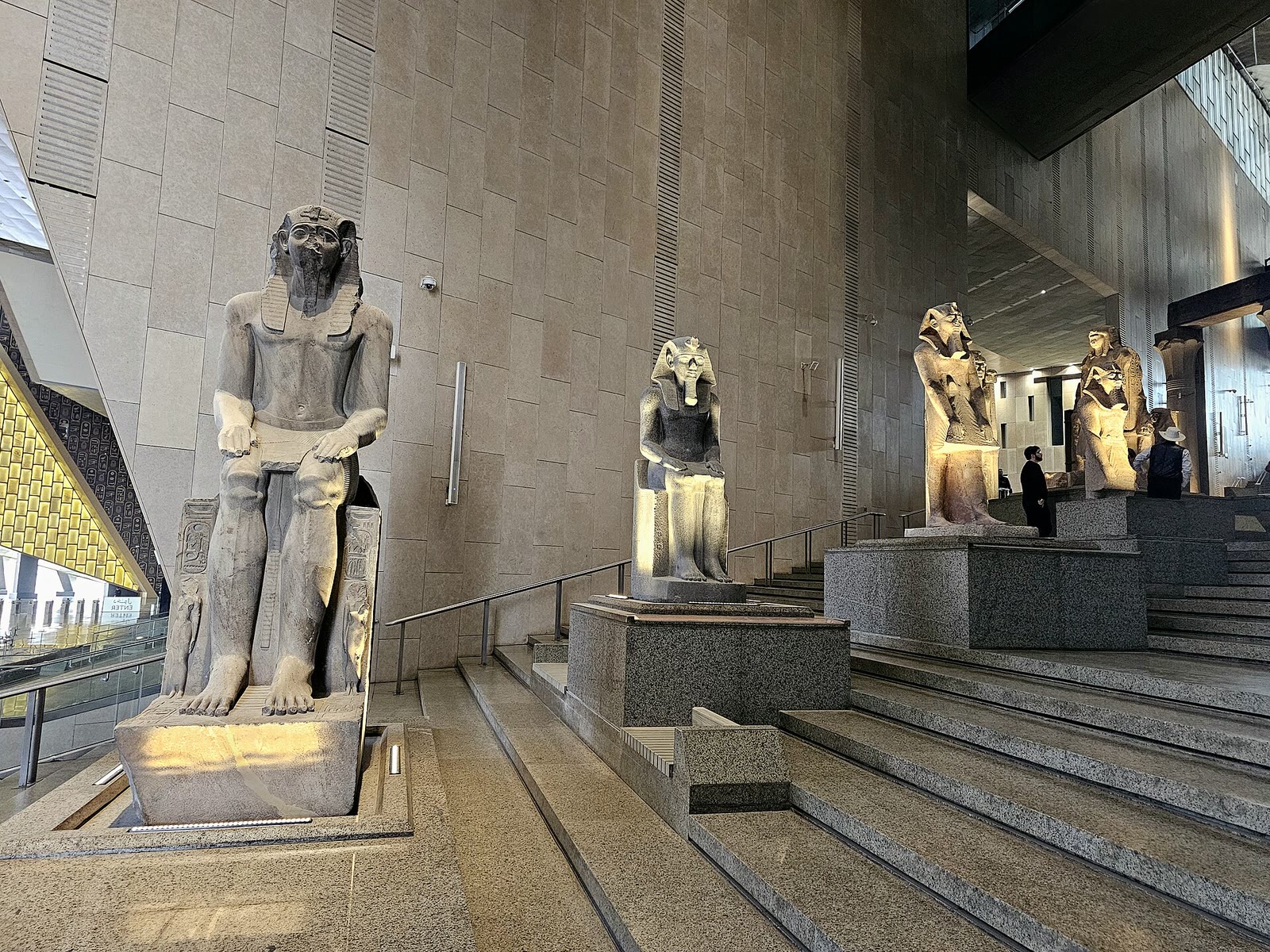 Visitors on the grand staircase lined with statues inside the Grand Egyptian Museum